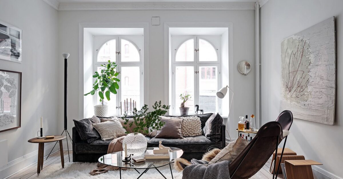 bright Scandinavian living room with large windows white walls black sofa leather armchair and plants